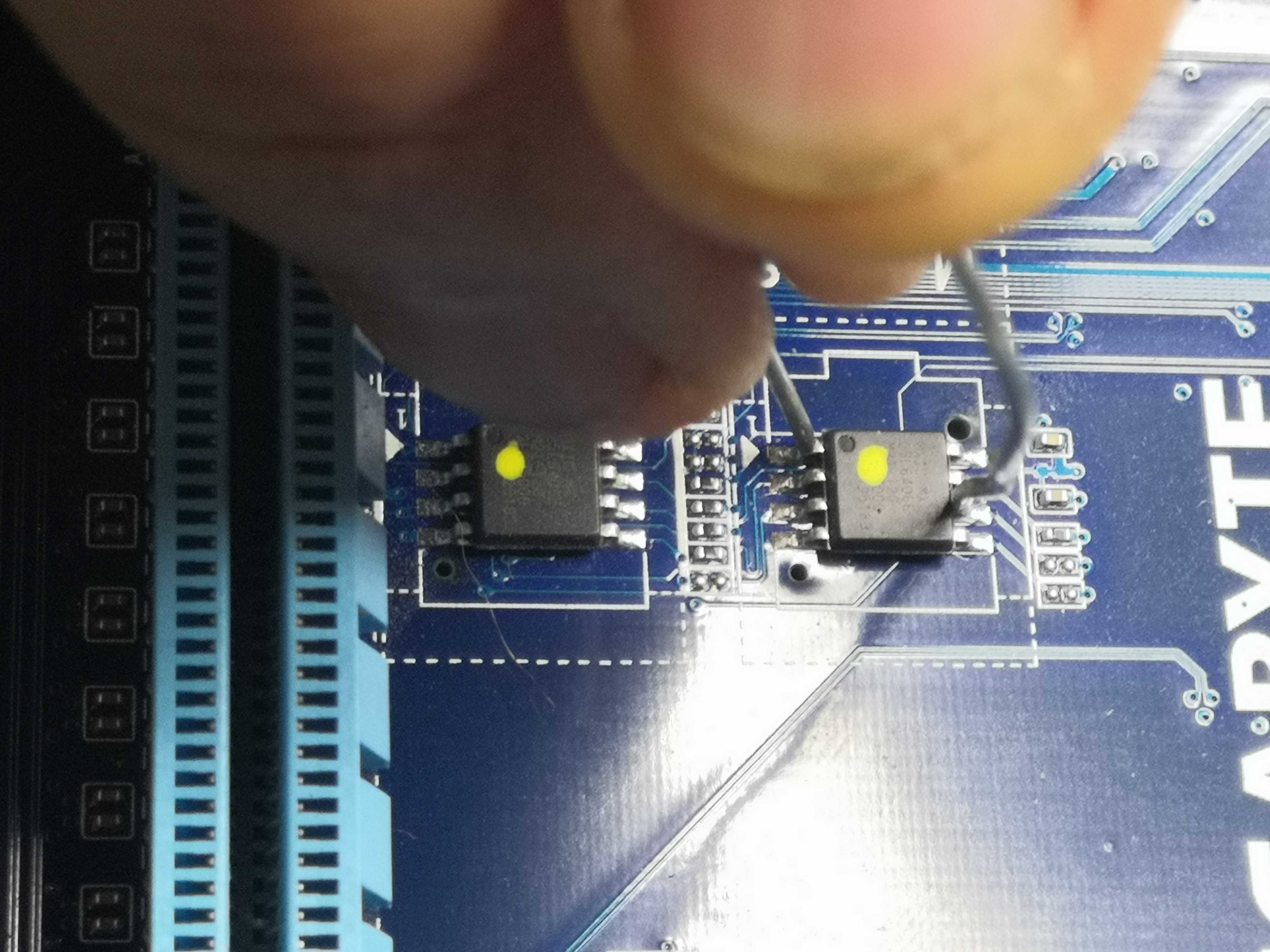 Close-up of the two BIOS chips — the jumper wire is visible between the legs of the M_BIOS on the right